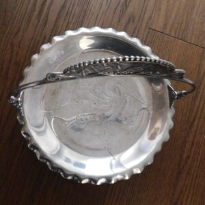 May include: Silver serving tray with a decorative handle and a scalloped edge. The tray has an embossed design on the bottom.