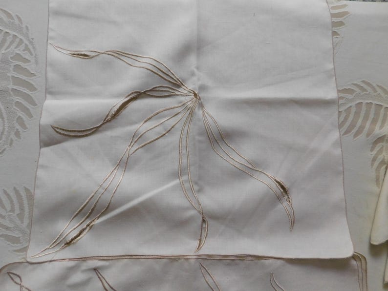 Pu&ograve; includere: Tovaglioli di lino bianco sporco con ricami floreali. Ogni tovagliolo presenta un motivo floreale centrale stilizzato in filo marrone chiaro. Il ricamo crea un motivo delicato e strutturato sul tessuto. I tovaglioli sono quadrati.