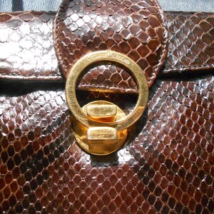 May include: A brown snakeskin handbag with a gold-toned clasp and the text "Valentino" engraved on the clasp.