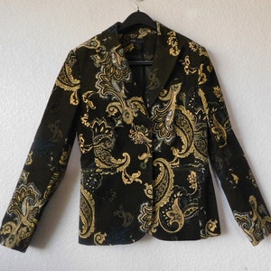 Puede incluir: Una chaqueta negra con estampado paisley dorado. La chaqueta tiene cuello de muesca, mangas largas y cierre de un solo botón.