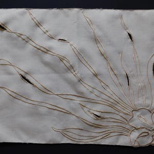 Pu&ograve; includere: Tovaglietta rettangolare color crema con un ricamo floreale. Il design presenta lunghe linee curve e un fiore nell'angolo in basso a destra. La tovaglietta ha dettagli ritagliati ed &egrave; probabilmente in lino.