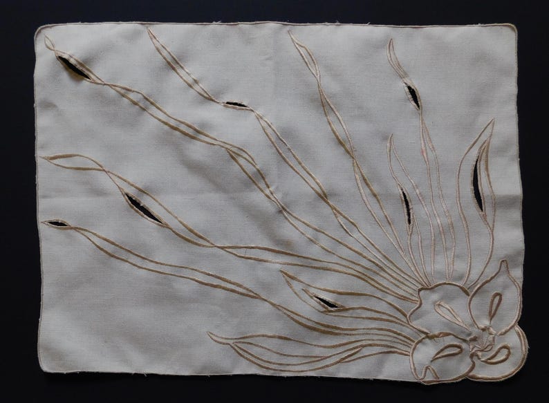 Pu&ograve; includere: Tovaglietta rettangolare color crema con un ricamo floreale. Il design presenta lunghe linee curve e un fiore nell'angolo in basso a destra. La tovaglietta ha dettagli ritagliati ed &egrave; probabilmente in lino.