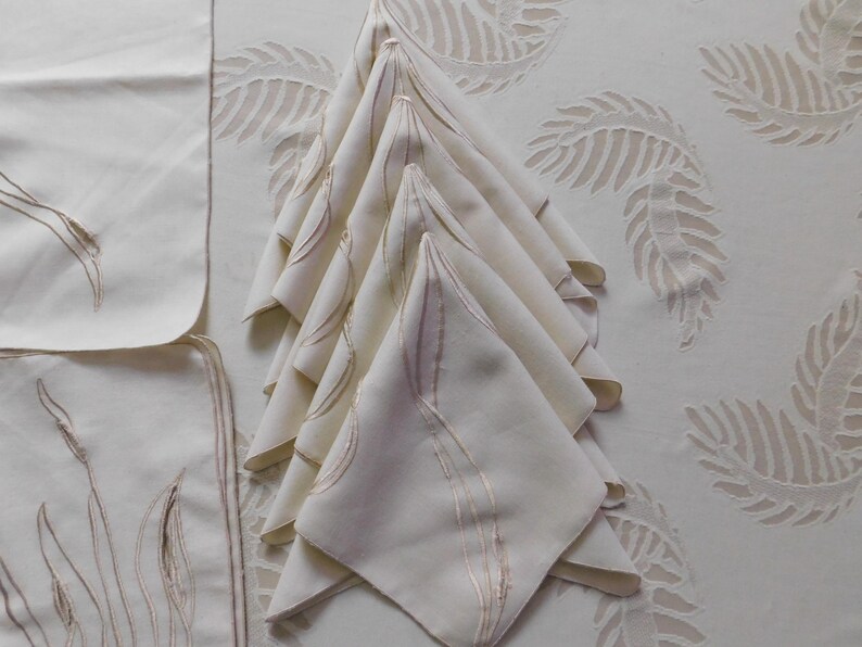 Pu&ograve; includere: Tovaglioli di lino color crema con un delicato design ricamato, impilati ordinatamente su una tovaglia abbinata. I tovaglioli presentano un sottile motivo a foglie, che completa il motivo a foglie pi&ugrave; grande sulla tovaglia. Un set di eleganti tovaglie.