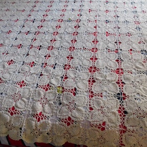 May include: White crocheted bedspread with a delicate floral pattern. The bedspread is laid out on a red and white striped bed.