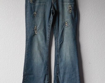 May include: Blue denim flared jeans with distressed details and rhinestones. The jeans have a mid-rise waist and a wide leg opening.