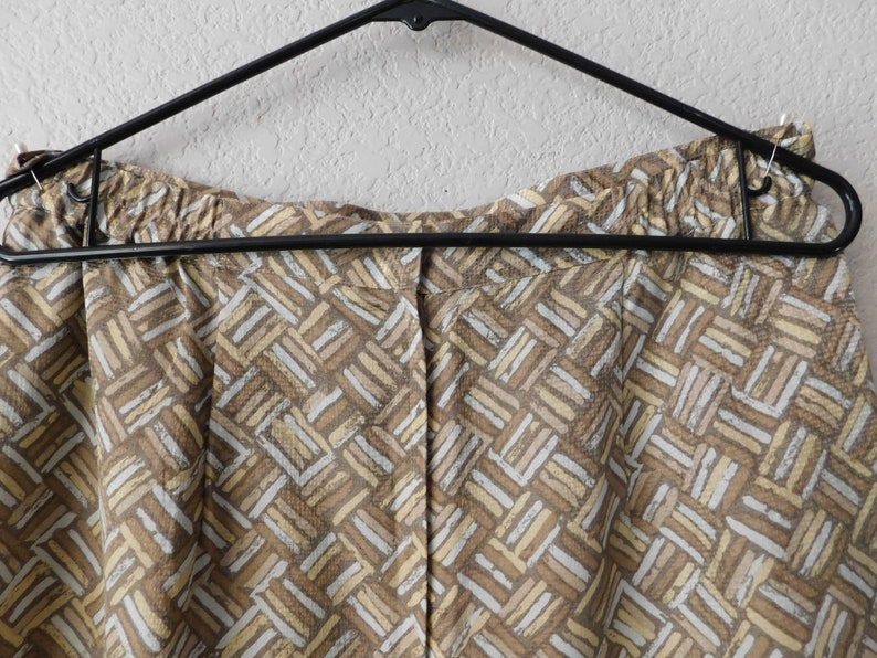 May include: Brown and beige patterned shorts with an elastic waistband. The shorts are hanging on a black hanger.