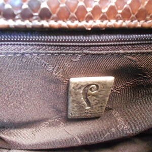 May include: Close-up of the interior of a brown leather handbag with a silver metal logo that reads "The  Original  Vivienne Westwood".