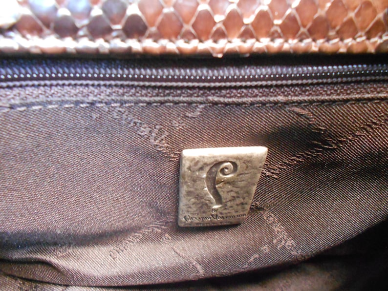 May include: Close-up of the interior of a brown leather handbag with a silver metal logo that reads "The  Original  Vivienne Westwood".