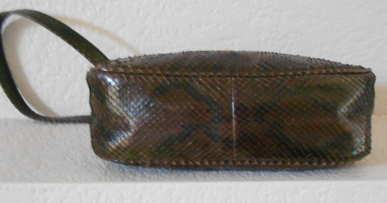 May include: A brown snakeskin handbag with a short strap. The bag has a textured, diamond-shaped pattern.