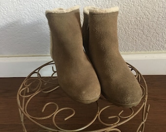 May include: A pair of brown suede ankle boots with a faux fur lining. The boots are sitting on a decorative metal stand.