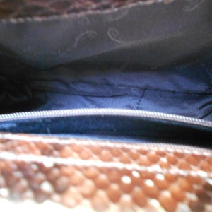May include: The inside of a brown snakeskin handbag with a zipper closure. The lining is a dark blue fabric.