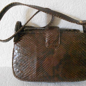 May include: A brown snakeskin shoulder bag with a flap closure and a gold-toned buckle. The bag has a long strap and a textured snakeskin pattern.