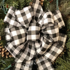 May include: A large, decorative bow made of black and white checkered fabric. The bow is surrounded by pine needles and pine cones, suggesting a holiday or seasonal theme. The text "Starr Events" is visible on the bow.