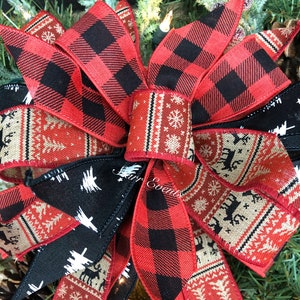 May include: A red and black plaid Christmas bow with a white and red patterned ribbon and a tan and red patterned ribbon. The bow is tied with a black ribbon.