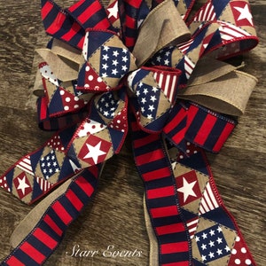 May include: A red, white, and blue patriotic bow with a burlap ribbon and a patchwork design featuring stars and polka dots. The bow is tied in a knot and has a frayed edge. The text "Starr Events" is visible in the lower center of the image.