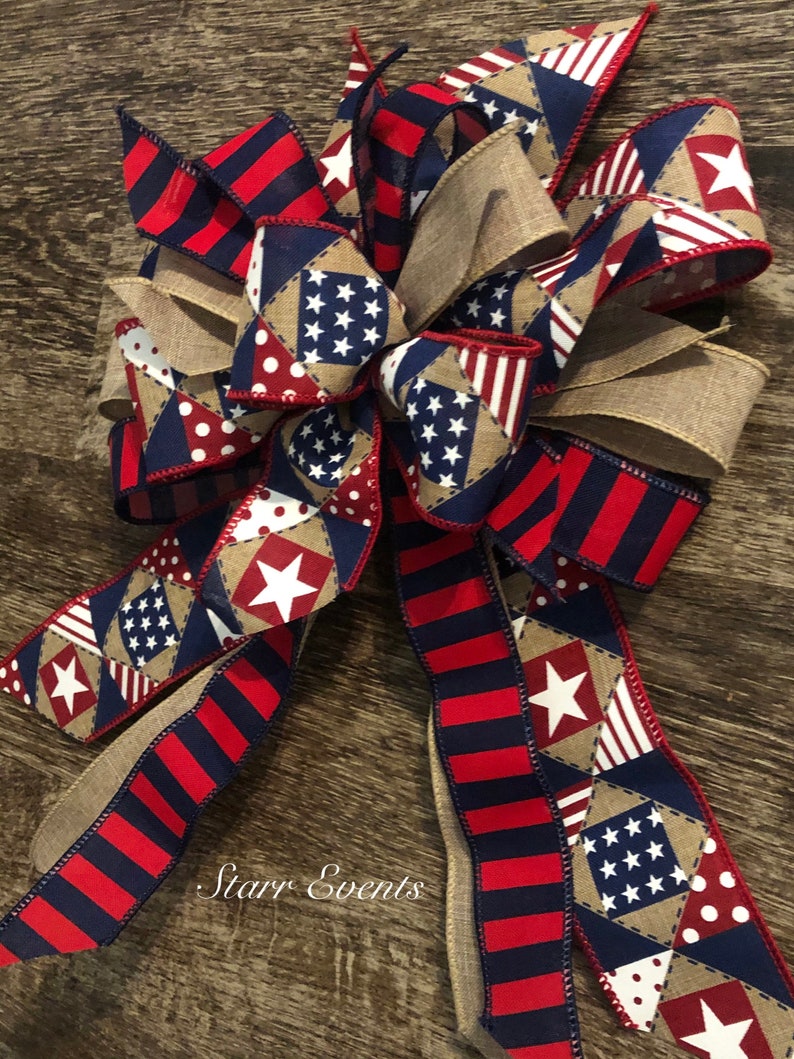May include: A red, white, and blue patriotic bow with a burlap ribbon and a patchwork design featuring stars and polka dots. The bow is tied in a knot and has a frayed edge. The text "Starr Events" is visible in the lower center of the image.