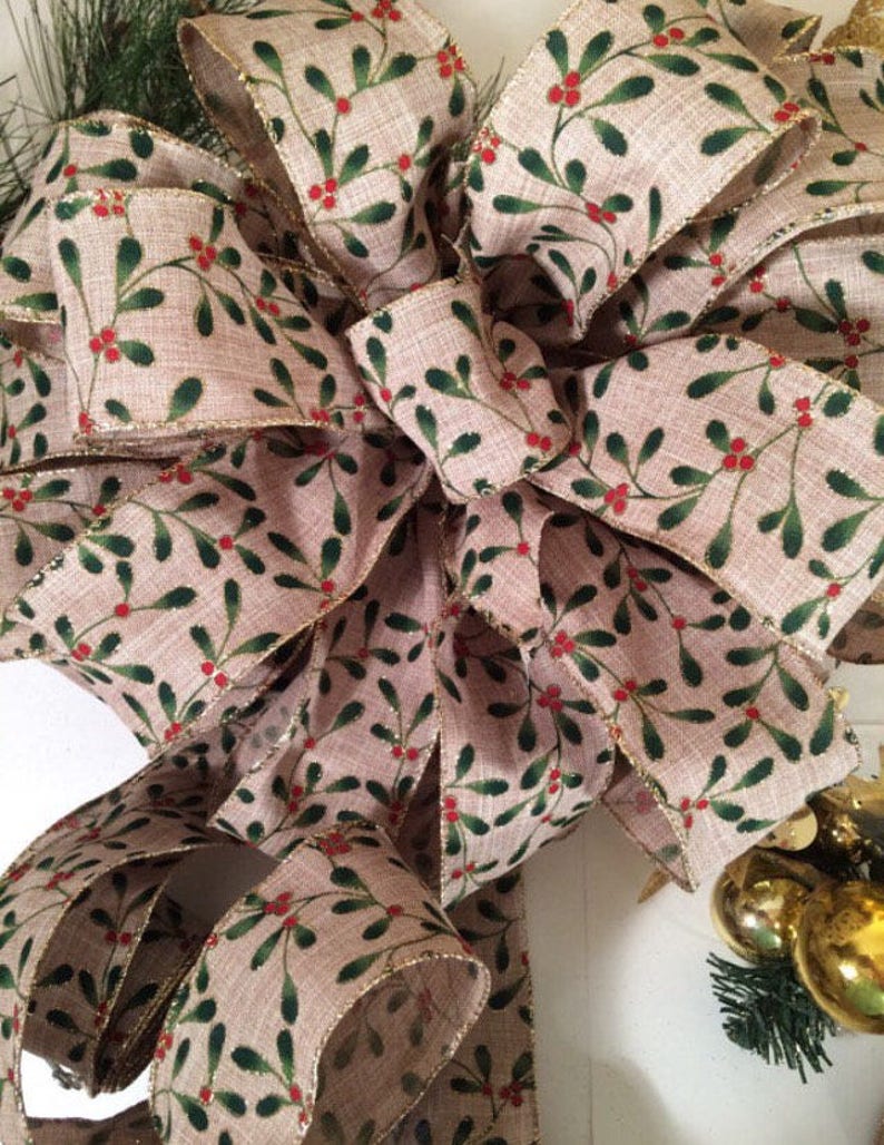K&ouml;nnte beinhalten: Eine gro&szlig;e, festliche Schleife aus Burlap-Band mit einem Muster aus gr&uuml;nen und roten Stechpalmenbeeren. Das Band hat einen goldenen Glitzerbesatz.