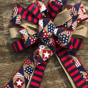 May include: A red, white, and blue patriotic bow with a burlap ribbon and a patchwork design featuring stars and polka dots. The bow is tied with a knot and has two long tails. The text "Starry Events" is visible on the bow.