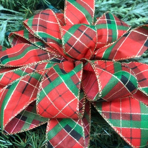 May include: A large, decorative bow with a red, green, black, and gold plaid pattern. The bow is made of fabric and has gold trim along the edges. The bow is likely for Christmas or holiday decorations.