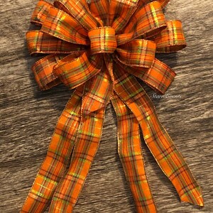 May include: A large orange and green plaid bow with a gold shimmer. The bow has four long tails.