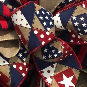 May include: A red, white, and blue patterned ribbon bow with stars, polka dots, and a burlap background. The bow is tied with a red ribbon.