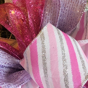 K&ouml;nnte beinhalten: Nahaufnahme eines rosa-wei&szlig; gestreiften Bandes mit silbernem Glitzer, einem rosa glitzernden Band und einem lila glitzernden Band. Die B&auml;nder sind in Form einer Schleife angeordnet.