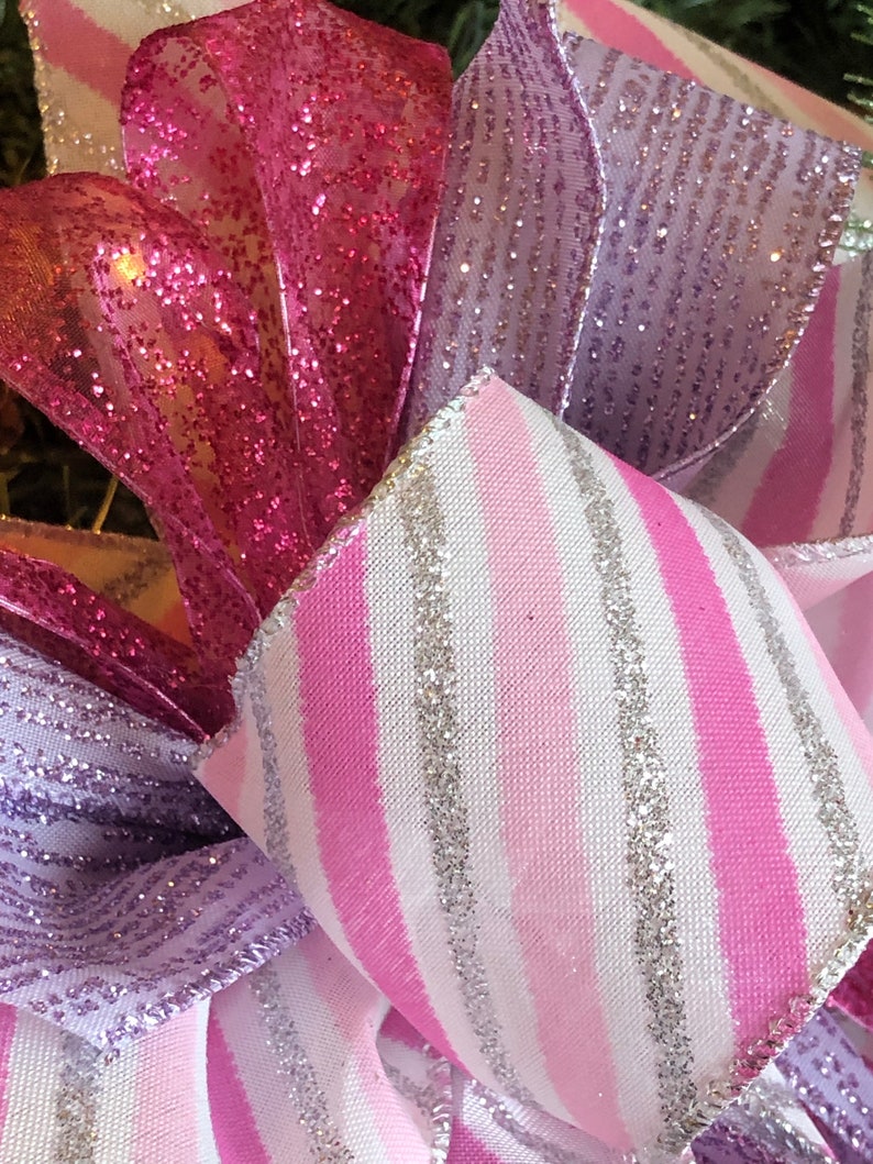K&ouml;nnte beinhalten: Nahaufnahme eines rosa-wei&szlig; gestreiften Bandes mit silbernem Glitzer, einem rosa glitzernden Band und einem lila glitzernden Band. Die B&auml;nder sind in Form einer Schleife angeordnet.