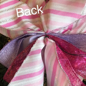 K&ouml;nnte beinhalten: Ein rosa-wei&szlig; gestreiftes Band mit silbernem Glitzerbesatz, ein lila Band mit silbernem Glitzerbesatz und ein rosa Band mit silbernem Glitzerbesatz und rosa Glitzer. Die B&auml;nder sind zu einer Schleife gebunden.