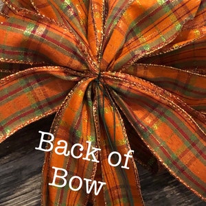 May include: Back of a large orange, green, and gold plaid bow with gold glitter. The bow is tied with a green wire.