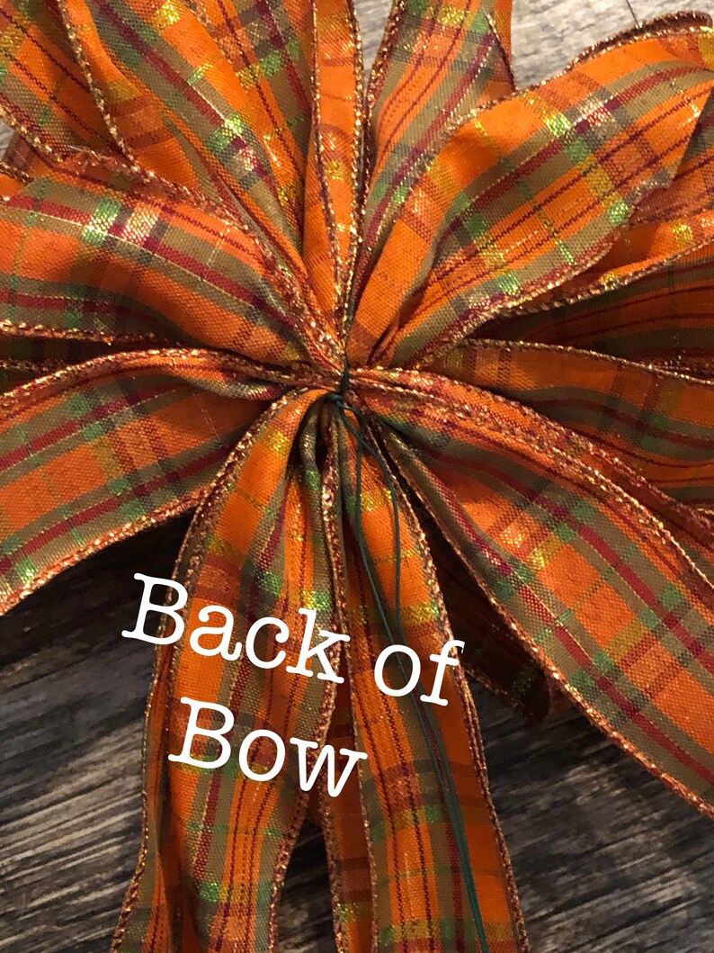 May include: Back of a large orange, green, and gold plaid bow with gold glitter. The bow is tied with a green wire.