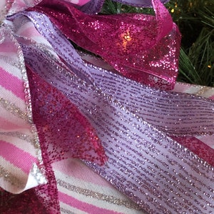 K&ouml;nnte beinhalten: Nahaufnahme eines rosa und violetten Bandes mit silbernem Glitzer. Das Band ist zu einer Schleife gebunden und hat ein wei&szlig;-rosa gestreiftes Muster.