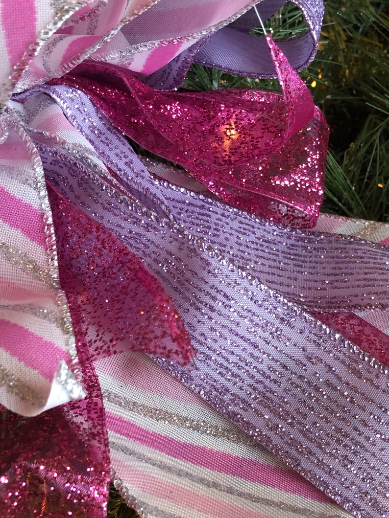 K&ouml;nnte beinhalten: Nahaufnahme eines rosa und violetten Bandes mit silbernem Glitzer. Das Band ist zu einer Schleife gebunden und hat ein wei&szlig;-rosa gestreiftes Muster.