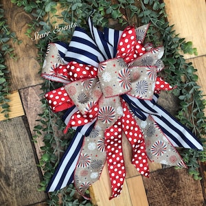 May include: A patriotic bow featuring red and white polka dots, navy blue stripes, and a beige ribbon with firework designs. The bow is set against a wooden background with greenery, perfect for festive decorations. The text "Starr Events" is visible.