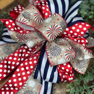 May include: A decorative bow featuring patriotic colors and patterns. The bow includes red and white polka dot ribbon, navy blue and white striped ribbon, and tan ribbon with a firework design. The bow is suitable for various decorative purposes.