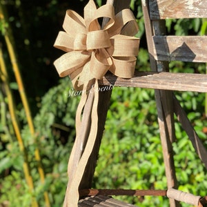 May include: A large, brown burlap bow with a long tail, tied to a wooden ladder. The bow is tied in a classic, symmetrical style with multiple loops.