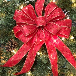May include: A large, bright red bow with gold accents, set against a backdrop of evergreen branches, berries, and twinkling lights. The bow has long, flowing tails and a textured pattern. The text "Starr Events" is visible.