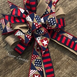 May include: A red, white, and blue patriotic bow with a burlap ribbon. The bow features a patchwork design with stars, stripes, and polka dots.