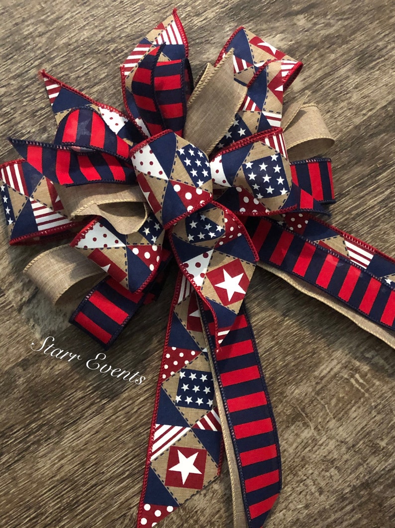 May include: A red, white, and blue patriotic bow with a burlap ribbon. The bow features a patchwork design with stars, stripes, and polka dots.