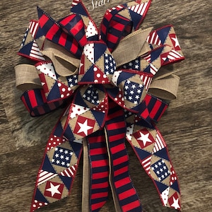 May include: A red, white, and blue patriotic bow with a burlap center. The bow is made of various fabrics with stars and stripes patterns.