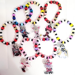 Peut inclure: Une collection de huit bracelets circulaires en perles de plastique colorées disposées en divers motifs. Chaque bracelet comporte une breloque en acrylique représentant un personnage de dessin animé et un petit pentagramme argenté.