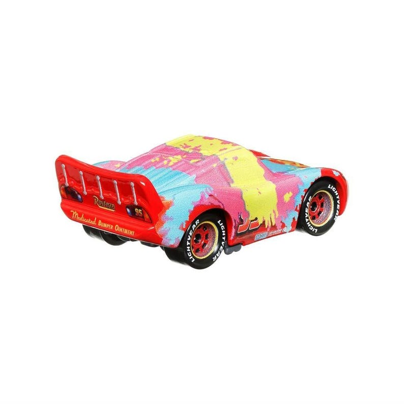 May include: A die-cast Lightning McQueen toy car with a colorful paint splatter design. The car is red with pink, yellow, and blue accents. The number 95 is visible on the side. The wheels are red with white lettering.