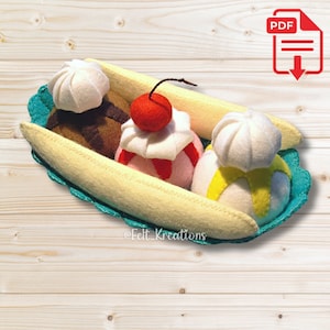 Puede incluir: Un banana split de fieltro con tres bolas de helado, una cereza en la parte superior y un plátano en un plato de fieltro azul. Las bolas de helado están cubiertas con crema batida y salsa de chocolate.