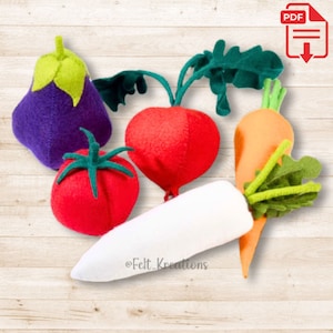 Puede incluir: Juguetes de fieltro en forma de verduras, incluyendo una berenjena morada, un tomate rojo, un rábano rojo, un rábano blanco y una zanahoria naranja. Las verduras están dispuestas sobre una superficie de madera.