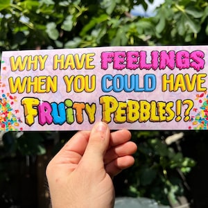 Może przedstawiać: Prostokątna naklejka z napisem "WHY HAVE FEELINGS WHEN YOU COULD HAVE FRUITY PEBBLES!?" w kolorowych literach na różowym tle. Naklejka ma obramowanie w kształcie konfetti.