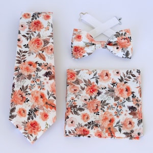 May include: A set of three matching accessories in a floral pattern. A tie, bow tie, and pocket square feature a white background with orange and brown floral designs.