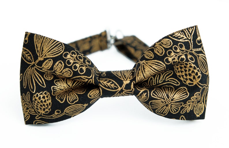 Puede incluir: Una pajarita negra con un estampado floral dorado.