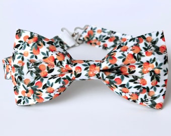 May include: A white bow tie with a floral pattern of orange citrus fruit and green leaves.