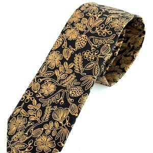 Puede incluir: Una corbata negra con un patr&oacute;n floral dorado. La corbata est&aacute; hecha de una tela lisa y tiene una punta puntiaguda.