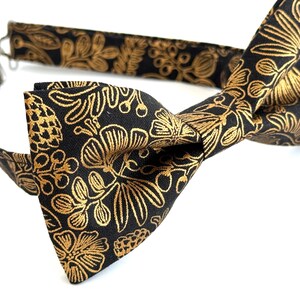 Puede incluir: Una pajarita negra con un patr&oacute;n floral dorado.