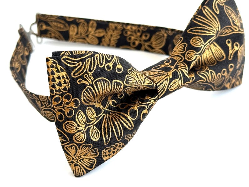 Puede incluir: Una pajarita negra con un patr&oacute;n floral dorado.